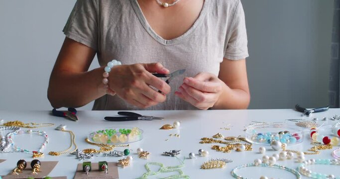 Female jewelry designer working in studio making necklace and earrings