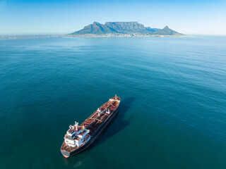 Cargo ship approaching Cape Town harbour on a clear, blue day, viewed from the stern. Table...