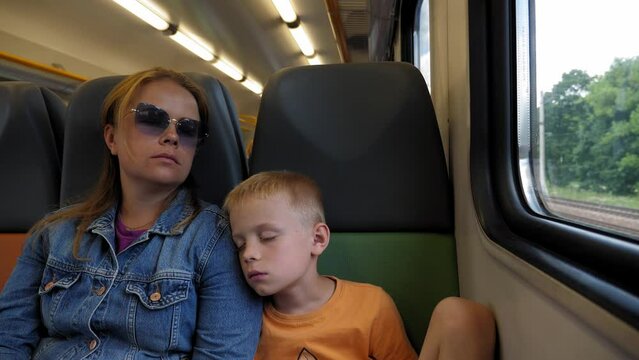 Tired mother and son sleep on the train during the trip, the boy leans on his mother. The family sleeps in chairs on the train in the summer.