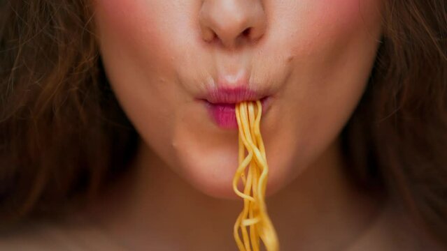 Portrait of Young Woman Eating Dinner Food on Camera Close Up. Crop Face of Modern Person with Instant Noodles on Sticks in Mouth. Hunger Lady with Good Appetite Bites Chinese Ramen Pasta in Studio