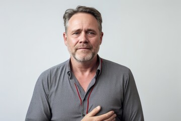 Medium shot portrait photography of a man in his 40s clutching his chest due to gastroesophageal reflux disease wearing a simple tunic against a white background 