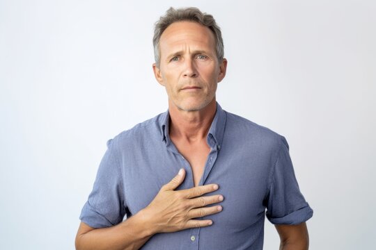 Medium shot portrait photography of a man in his 40s clutching his chest due to gastroesophageal reflux disease wearing a simple tunic against a white background 