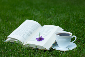 otwarta książka z kwiatem na trawie i filiżanka kawy
