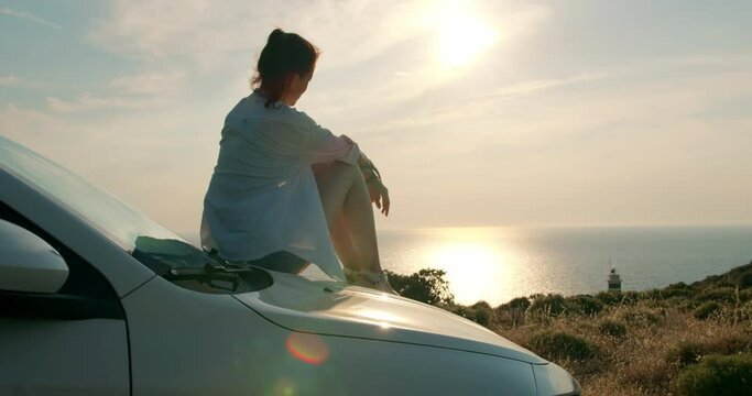 Young woman sitting on her car enjoying warm sunset view. escape into nature