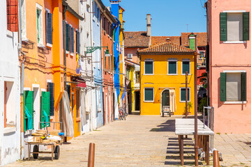 Fototapeta na wymiar Colourful houses and buildings on a quiet courtyard. Bright green shutters for the windows and clothes lines or wash lines with laundry. Burano, Venice, Italy. Empty table and chairs. 
