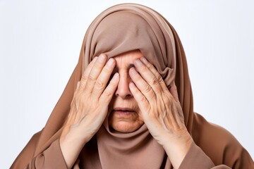Medium shot portrait photography of a woman in her 60s appearing tired and down due to hypothyroidism wearing hijab against a white background 