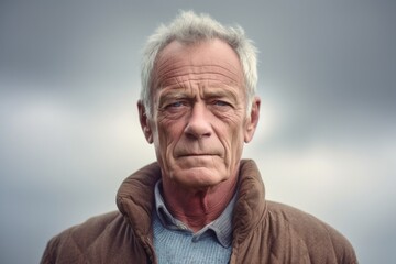 Medium shot portrait photography of a man in his 60s with a somber and deeply sad expression due to major depression wearing a chic cardigan against a sky and clouds background 