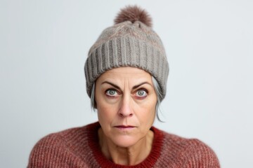 Medium shot portrait photography of a woman in her 50s looking anxious and fidgety due to generalized anxiety disorder wearing a warm beanie or knit hat against a white background 