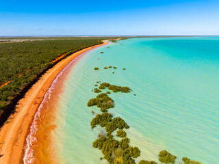 Aerial view of red sandy coastline along turquoise water at Red Sand Beach, Roebuck Bay, Broome, Western Australia