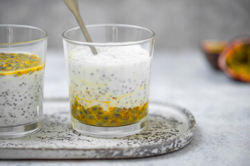 Chia pudding with passion fruit puree and yogurt in a glass on a grey background. Healthy vegetarian food. Tasty breakfast idea.