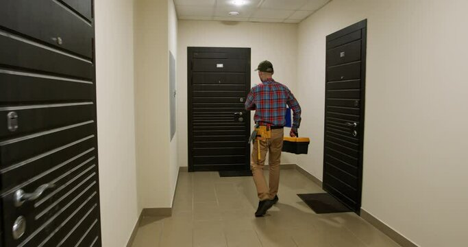 Male repair service worker knocks on door of client apartment. Concept of providing services at home. Man waits with tools kit in hands in corridor