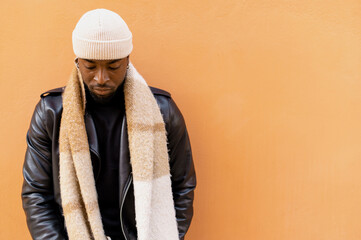 Thoughtful African American male wearing black leather jacket scarf and hat covering face with mask...