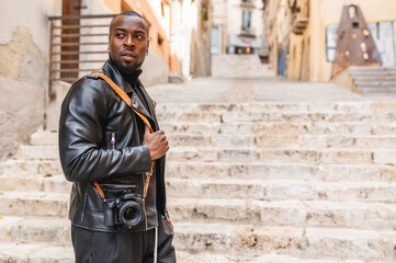 Fototapeta na wymiar Side view of trendy African American male photographer standing with modern photo camera in street of old city and looking away