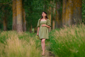 Caucasian Young Pregnant woman Tummy belly  summer green dress touching stomach field expecting a baby relaxing outside nature park lake rural Beautiful magic 8 months enjoying life glasses hat