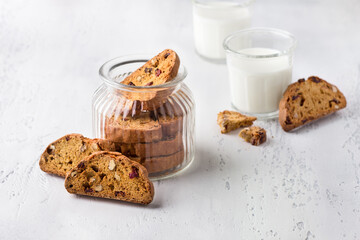 A glass jar of pumpkin biscotti with cranberries and nuts on light gray textured background. Delicious homemade food