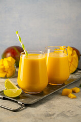 Mango smoothie in a glass with fresh mango on background.