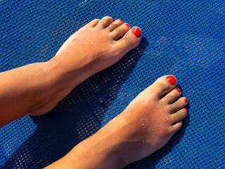Two feet tanned with red polish on a blue deckchair