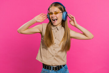 Happy woman in headphones listening music and dancing disco fooling around having fun expressive gesticulating hands relaxing on party. Blonde girl in sunglasses isolated on studio pink background