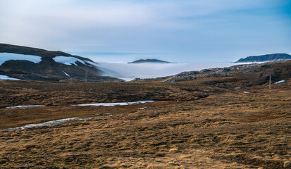 Beautiful tundra landscape with dry grass, some snow and fog in the valleys