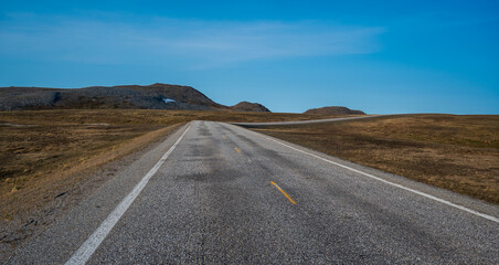 Asphalt road in beautiful tundra landscape with dry grass and some snow