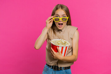 Excited young woman in 3D glasses eating popcorn and watching interesting tv serial, sport game, film, online social media movie content. Blonde lovely girl isolated on pink studio background