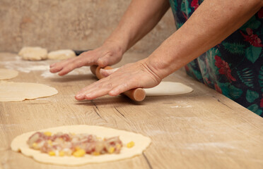 A woman rolls out the dough with a rolling pin on the table