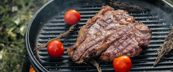 Beef T-Bone steak grilled porterhouse steak on barbecue grill with smoke and flames in green grass