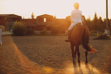 Woman rider jockey in helmet and white uniform preparing horse racing at sunset ranch