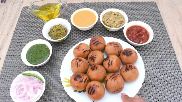 Litti in white plate with tomato, brinjal, potato, pointed gaurd and coriander chutney or chokha and ghee. It is popular in Bihar, Uttar Pradesh and Jharkhand.