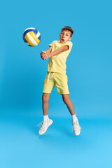 Funny and emotional boy, child in casual clothes playing beach volleyball against blue studio background. Concept of childhood, kids emotions, holiday, summer, fun and joy, ad