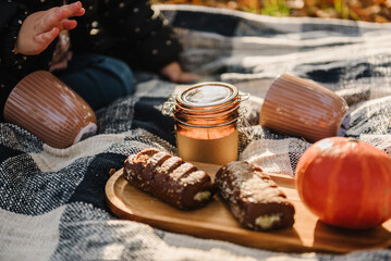 Autumn picnic. Pumpkin, coffee, sweets and candle. Picnic in autumn forest in nature. Child play on blanket on yellow leaves in park with sunlight. Family spending time together at sunset. Mood photo.