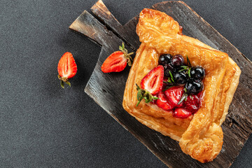 square fruit filled French puff pastry dessert with berries on a dark background. banner, menu, recipe place for text, top view