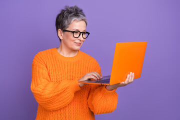 Photo of old pensioner woman orange pullover holding new netbook concentrated working remote...