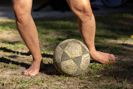 Pernas de mulher iluminadas pela luz do sol jogando futebol, tocando a bola com o p&eacute; de lado em campo de futebol com gramado gasto. 