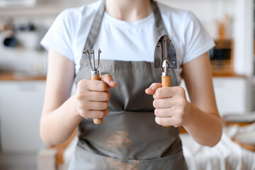 Woman gardener in grey apron holding garden utensils. Ready to work