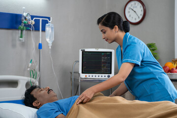 Indian nurse covering blanket to hospitalized sick patient by talking at ward - concept of medicare...