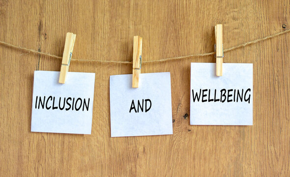 Inclusion and wellbeing symbol. Concept words Inclusion and wellbeing on beautiful white paper on clothespin. Beautiful wooden background. Motivational inclusion and wellbeing concept. Copy space.