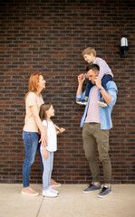 Family with a mother, father, son and daughter standing by the wall of brick house