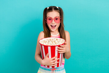 Photo of charming astonished girl hold big popcorn box open mouth heart shape sunglass isolated on teal color background