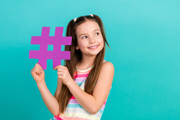 Photo of funny small girl arms hold paper hashtag symbol look empty space isolated on teal color background