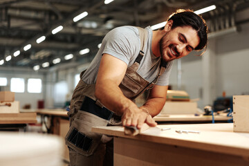 Young carpenter making wood furniture while working in joinery