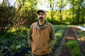 A young farmer hipster stands confidently in a lush green field, exuding a sense of connection to nature and a modern aesthetic. 