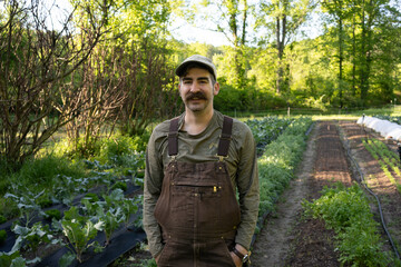 A young farmer hipster stands confidently in a lush green field, exuding a sense of connection to nature and a modern aesthetic. 