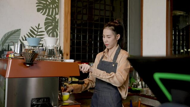 Asian woman shop owner, machine with finely ground coffee is being introduced coffee machine, hold coffee use hot coffee mug support brewing coffee, before making menu according customer's order.
