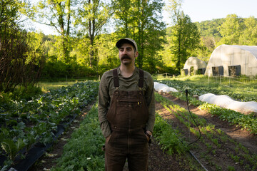 A young farmer hipster stands confidently in a lush green field, exuding a sense of connection to nature and a modern aesthetic. 
