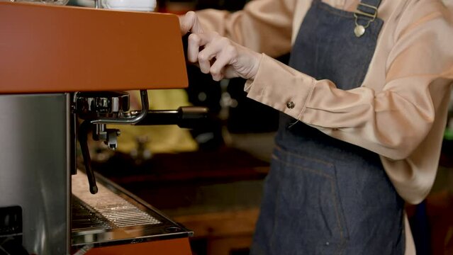 Close-up hand Asian woman shop owner, who is working as barista in own cafe, is bringing machine that contains pre-ground coffee assemble coffee maker, making menus according customer orders.