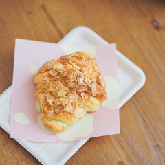 Croissant. A top view of almonds croissant on the wooden table, served in takeaway paper dish. Soft focus.