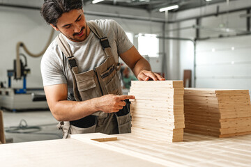 Young carpenter man looking and choosing wood plank at workshop in carpenter wood factory