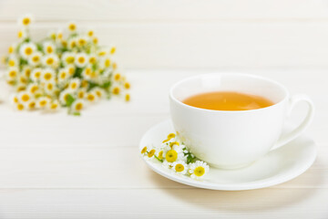 Obraz na płótnie Canvas Chamomile tea on a white table. Delicious tonic, soothing and relaxing chamomile tea with chamomile flowers, honey and lemon. Herbal tea for immunity. Close-up.Place for text.Copy space.