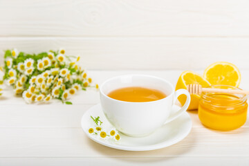 Chamomile tea on a white table. Delicious tonic, soothing and relaxing chamomile tea with chamomile flowers, honey and lemon. Herbal tea for immunity. Close-up.Place for text.Copy space.